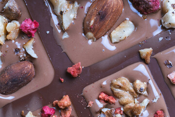 The process of making homemade chocolate. Nuts, freeze-dried raspberries and strawberries are laid out on liquid chocolate.