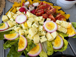 Traditional Easter food platter with cheese cubes, hard-boiled eggs, fresh vegetables and lettuce, served on a festive table.