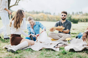 A group of friends unwinding during a casual picnic in the countryside, sharing food and laughter under a tree with a backdrop of nature's beauty.