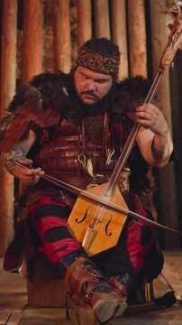 Yakut musician in traditional suit plays igil by bow at folk art concert on stage. Altai man presents ancient spiritual melody. Local culture
