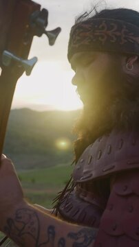 Concentrated plump musician plays igil with bow against mountain at sunrise close side view. Presenting old Altai melodies. Siberian culture festival