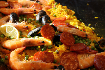 Cooking seafood paella with shrimp, mussels, calamari, chicken and chorizo shiny in the rays of the morning sun close up.