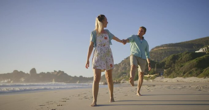 Couple, travel and walking by ocean, love and talking on vacation for romance on honeymoon. People, holding hands and playful on tropical island, support and drag husband by waves on weekend date