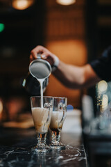 A barista delicately pours warm milk into clear glass mugs on a polished marble countertop under soft ambient lighting, creating a cozy and inviting coffee shop atmosphere.