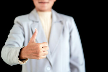 woman wearing suit showing thumb finger with black background. female person reveal hand sign with thumb finger out performing something. young adult woman giving thumb point from hand showing sign