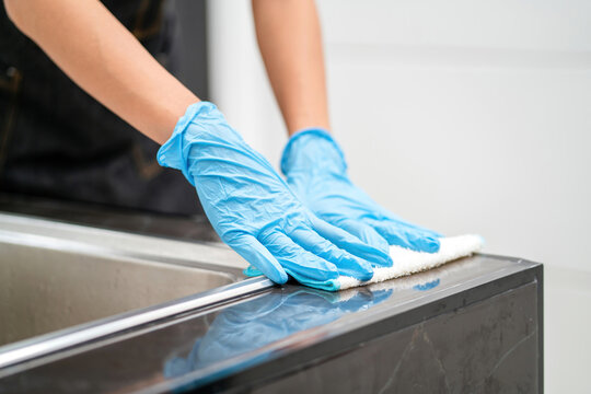 female house cleaner working cleaning counter wearing gloves using rag. housekeeper service doing chores disinfect kitchen surface with towel. professional housework staff woman cleaning sink counter
