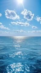 Obraz premium Sunlit ocean horizon under a bright blue sky with scattered clouds.