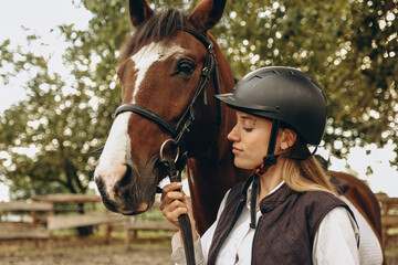 A young female equestrian stands near her horse and prepares for a competition.