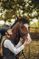Fototapeta premium A young female equestrian stands near her horse and prepares for a competition.