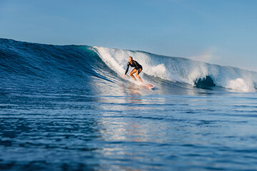 Surfer woman riding on ideal blue wave on a sunny day, surfing in ocean.