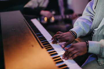 Fototapeta premium A musician's hands playing the piano in an intimate setting, capturing creativity and concentration. The background shows another musician with a guitar, adding to the collaborative ambiance.
