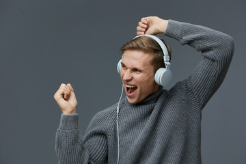 Joyful young man wearing headphones celebrating with clenched fist on plain gray background. Casual...