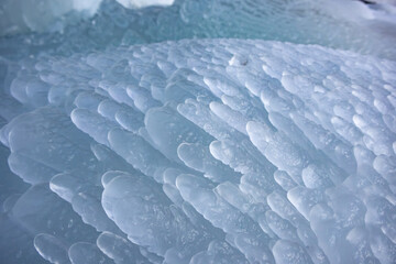 Close-up of a natural ice texture with layered, translucent formations. Abstract winter background with frozen, rounded shapes resembling frozen waves.