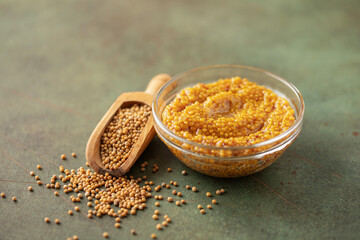 Mustard sauce in a bowl and seeds on a green background.