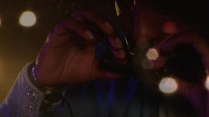 Male musician performing on music stage, showing harmonica with floating purple amber bokeh lights - Powered by Adobe