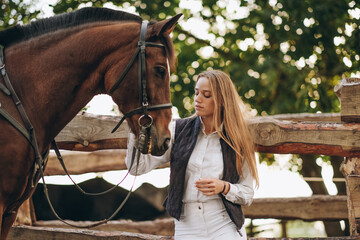 A young female equestrian stands near her horse and prepares for a competition.