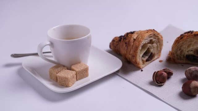 Tazza di caff&egrave; sul piattino con zollette di zucchero, e brioche alle mandorle sul tovagliolo