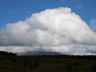 Large fluffy clouds drift over rolling hills under a blue sky during the afternoon