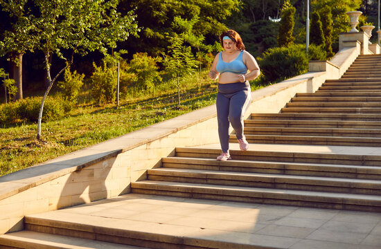 Plus size, fat woman is jogging up stairs in city park, engaging in outdoor training or sport running. Overweight woman commitment to fitness highlighting importance of run exercise and health.