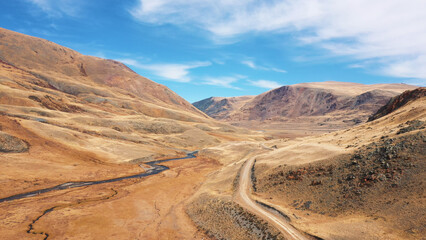 Fototapeta premium Aerial flying forward over picturesque mountain valley with ground road and curved river. Fabulous wildlife landscape in desert dry area. Go on trip around world. Wild hilly steppe or prairie