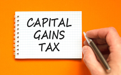 Capital gains tax symbol. Concept words Capital gains tax on beautiful white note. Beautiful orange background. Businessman hand with pen. Business and capital gains tax concept. Copy space.