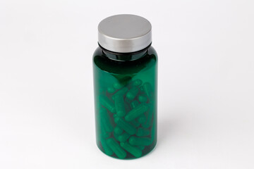Green Supplement Bottle Surrounded by White Capsules, Green bottle with a silver cap placed on a white background.