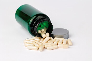 Spilled capsules from green bottle on white background, Close-up of beige capsules spilling out of a green plastic bottle onto a clean white background, representing supplements and healthcare.  