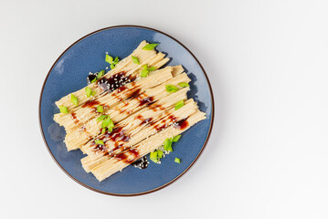 Tofu skin or yuba with green onions, sauce and sesame seeds in a blue plate.  Asian dish isolated on white background