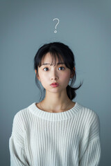 Young woman in white sweater with puzzled expression and question mark above head on grey background, great for problem-solving and decision-making visuals.