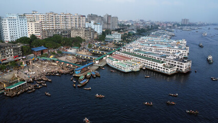 Dhaka is located on the banks of the Buriganga river. Aerial view of Sadar Ghat and the Buriganga river with modern cityscape and boats, Dhaka, Bangladesh.