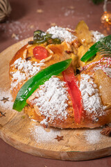 Colorful candied fruits and powdered sugar on a traditional Bolo Rei or Kings Cake, set on a wooden board amidst warm holiday decorations and lights. Is tradicional for Christmas in Portugal