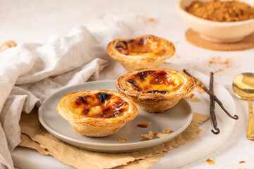 Three Pastel de Nata, Portuguese custard tarts, are presented on a plate with cinnamon and vanilla beans.