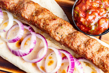 Savory kebab with onions and salsa on a wooden platter