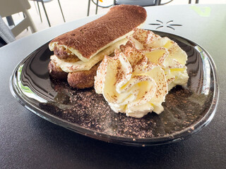 Creamy tiramisu dessert with whipped cream and cocoa on black plate