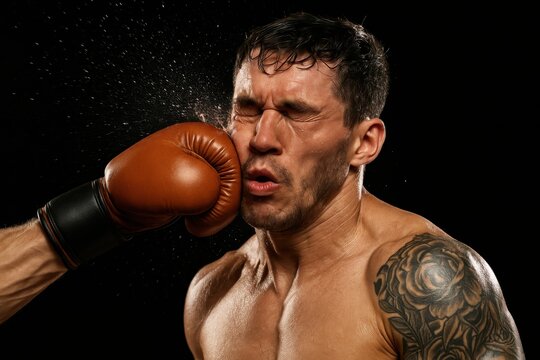 A boxer receives a powerful punch to the face, showing the sheer intensity and physicality of the sport, with sweat flying in the air under bright lights that illuminate the boxing ring