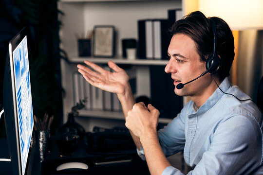 Call center consulting with customers on headphones on monitor in business paragraph with typing on pc with dynamic data marketing analysis planning at modern home office at night time. Pecuniary.