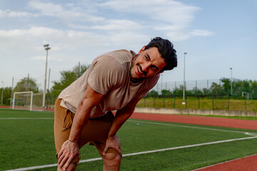 Exhausted male athlete resting on a stadium track, catching breath after an intense workout,...