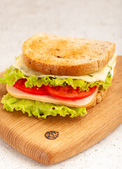A delicious sandwich layered with fresh lettuce, ripe tomato slices, and cheese sits on a wooden cutting board. Its golden-brown bread beckons for a satisfying lunch experience.