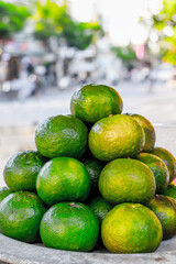 Fresh green oranges stacked outdoors in a vibrant urban market setting