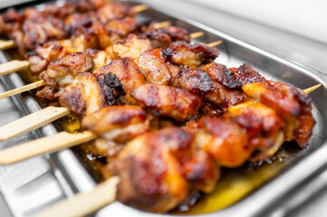 A close-up of grilled chicken skewers glistening with marinade, displayed in a stainless steel tray, showcasing appetizing barbecue cuisine.