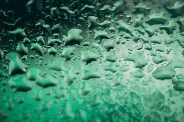 Close-up view of green-tinted water droplets on a glass surface, forming organic, fluid patterns, creating a textured and atmospheric background with copy space.