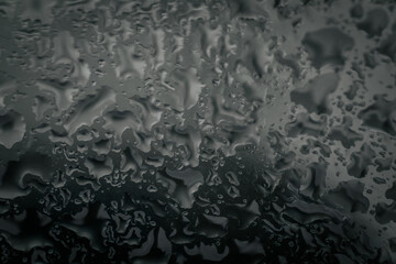 Close-up of water droplets creating abstract, organic patterns on a gray-toned glass surface, providing a moody and textured background with copy space.