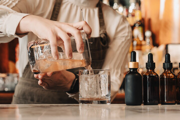 Bartender Pouring Cocktail over Ice at Bar