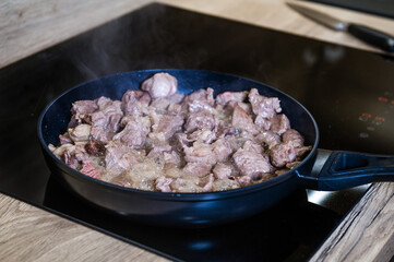Close up of meat cooking in a frying pan with steam. A frying pan on an induction cooker preparing meat for Pilaf. Cook recipe step-by-step.