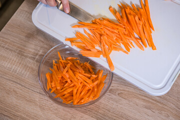 The women's hands place the chopped carrots in a glass bowl. Pilaf recipe in pictures. Cooking step.