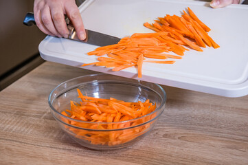 The women's hands place the chopped carrots in a glass bowl. Pilaf recipe in pictures. Cooking step.