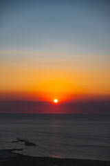 The sun at orange sunset just above the surface of the sea
