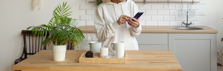Banner senior woman standing in the kitchen using a smartphone. Daily technology use and modern senior lifestyle. Copy space