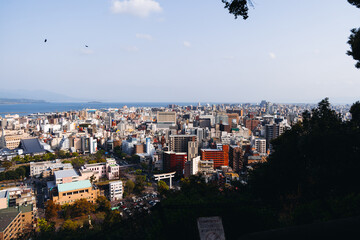 View of Kagoshima city, Japan, Kagoshima prefecture, Kyushu island region, with Sakurajima island volcano and Kagoshima bay, seen from Shiroyama park mountain observatory in a spring day with blue sky