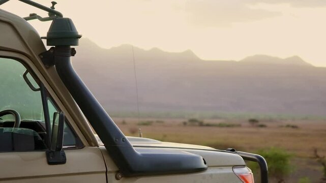 Safari game drive vehicle or 4x4 truck by sunset view in Tanzania Africa park. Sun setting or rising behind mountain ridge with special car for game view trip parked on hill or valley outdoors